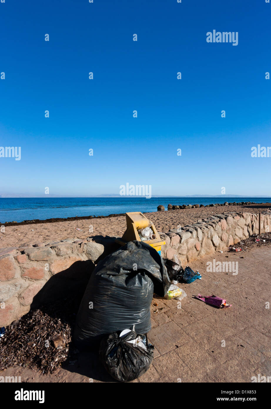 Overflowing abandoned bins and garbage bags left next to a tropical beach Stock Photo