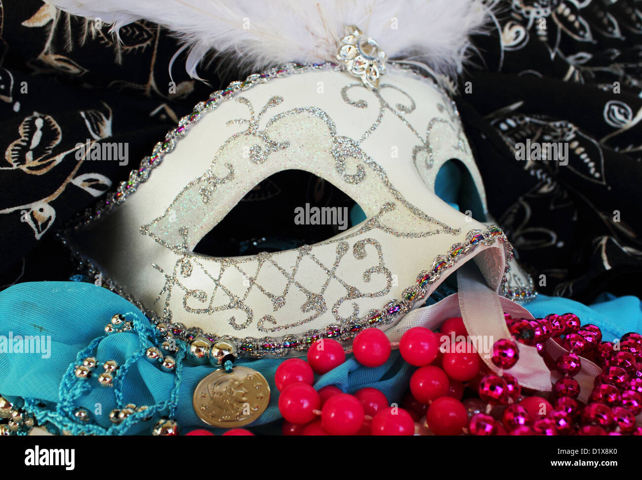 A masquerade ball mask adorned with glitter and rhinestons surrounded by party beads, bangles and fabrics Stock Photo