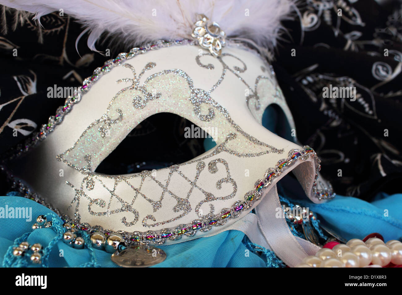 A masquerade ball mask adorned with glitter and rhinestons surrounded by party beads, bangles and fabrics Stock Photo