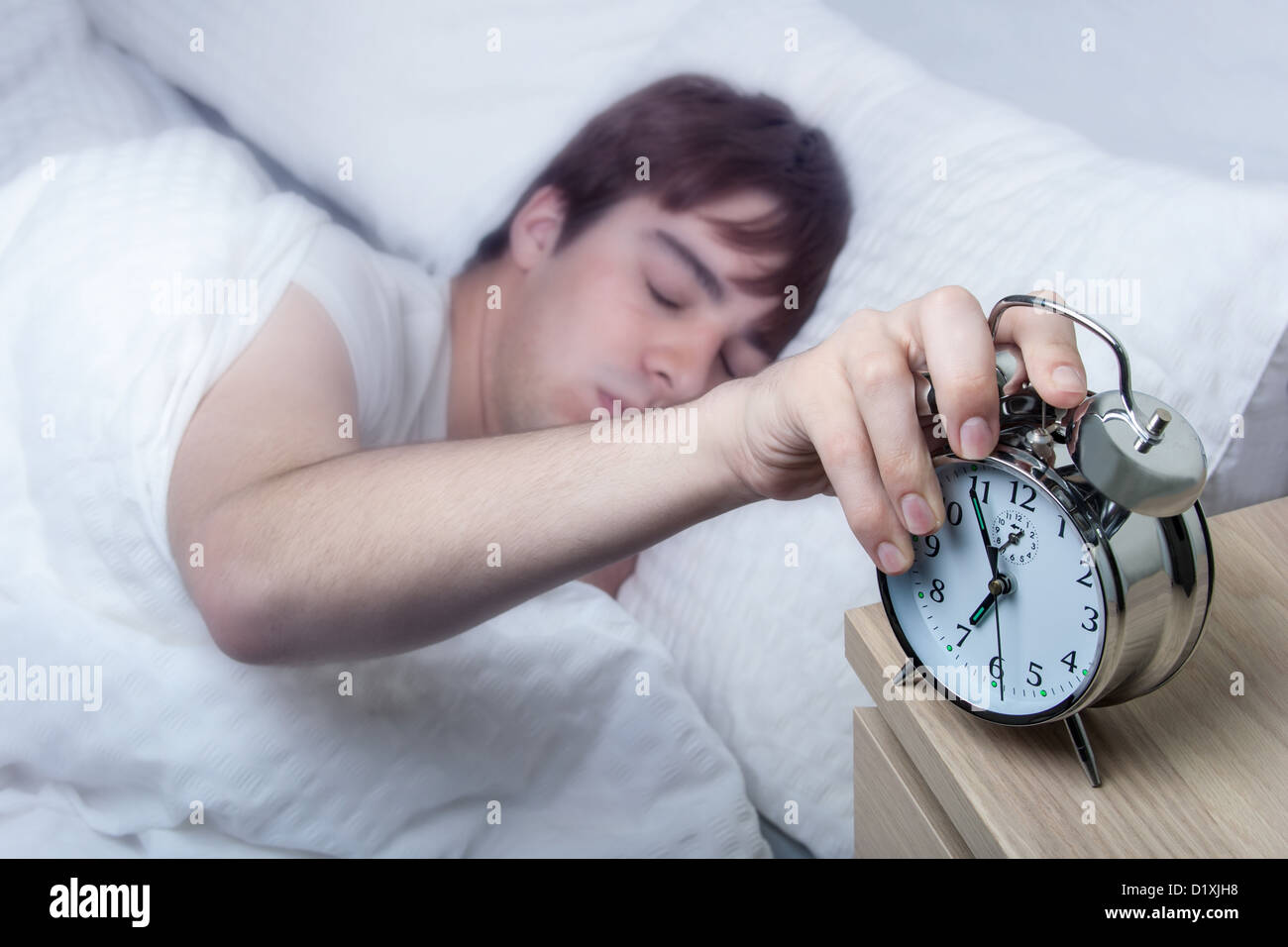Close up of an old fashioned alarm clock, young man turning it off still half asleep. Stock Photo