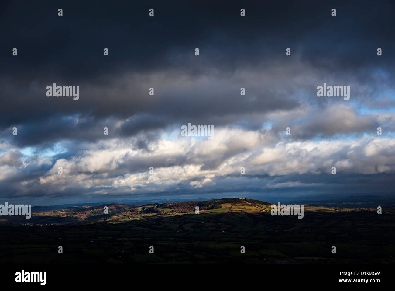 Dark skies over fields and moors lit through a gap in the clouds, from the Skirrid, Wales, UK Stock Photo