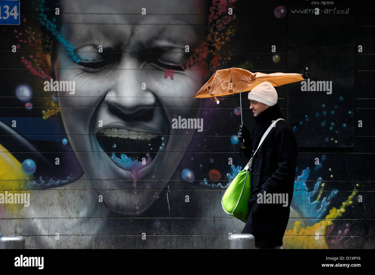 A pedestrian walks past a painted wall in a rainy day in Central Tel Aviv Israel Stock Photo