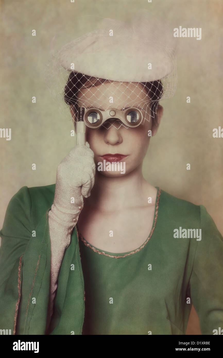 a woman in a green dress with hat is looking through a lorgnette Stock Photo