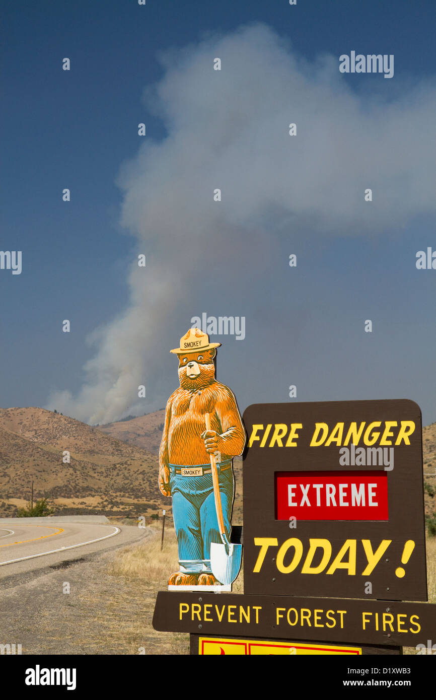 Smokey Bear extreme fire danger sign with a plume of smoke from a forest fire in the back ground in Boise County, Idaho, USA. Stock Photo