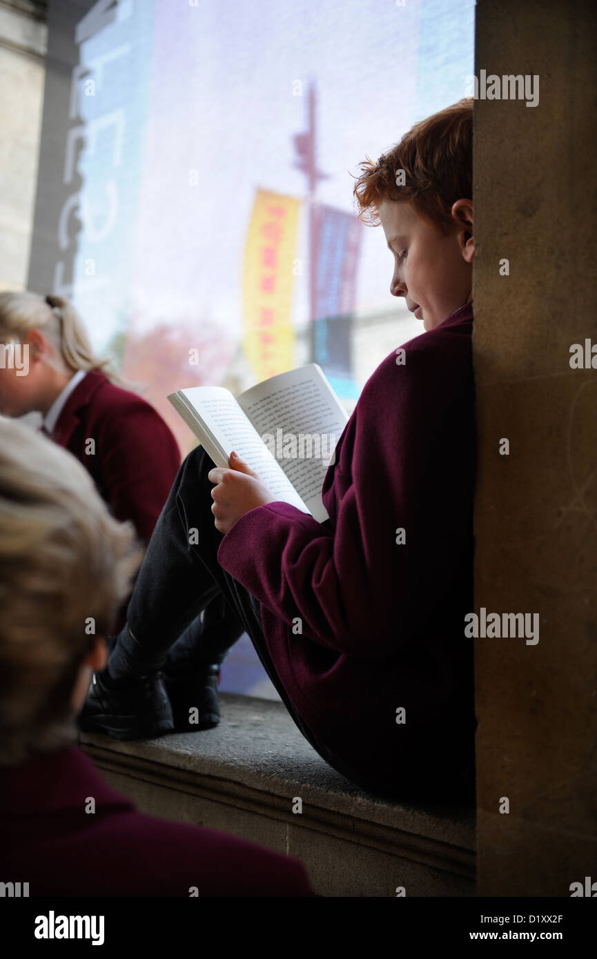 Children from Dean Close Preparatory School, Cheltenham reading at the Town Hall as they wait for buses after an event with the Stock Photo