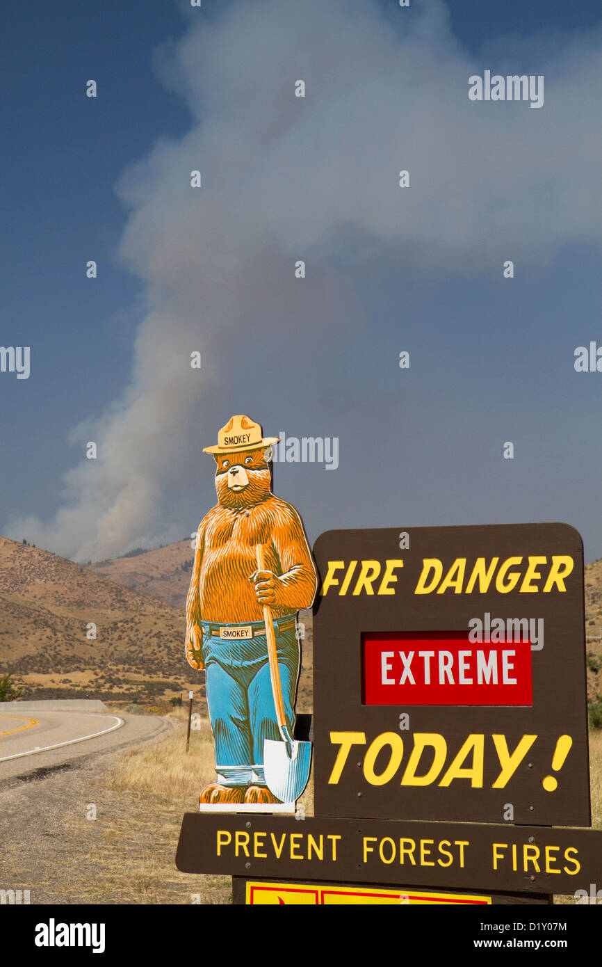 Smokey Bear extreme fire danger sign with a plume of smoke from a forest fire in the back ground in Boise County, Idaho, USA. Stock Photo