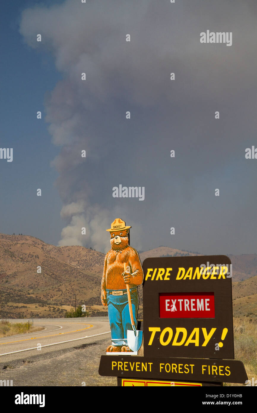 Smokey Bear extreme fire danger sign with a plume of smoke from a forest fire in the background in Boise County, Idaho, USA. Stock Photo