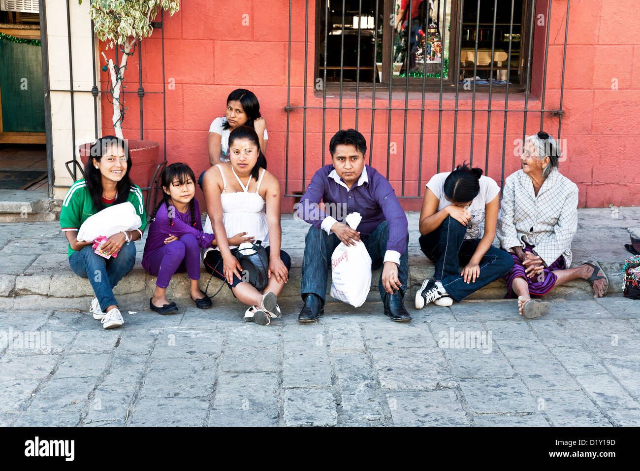 Mexican family members including grandmother & little girl touching her mother's baby belly sitting on curb Oaxaca Mexico Stock Photo