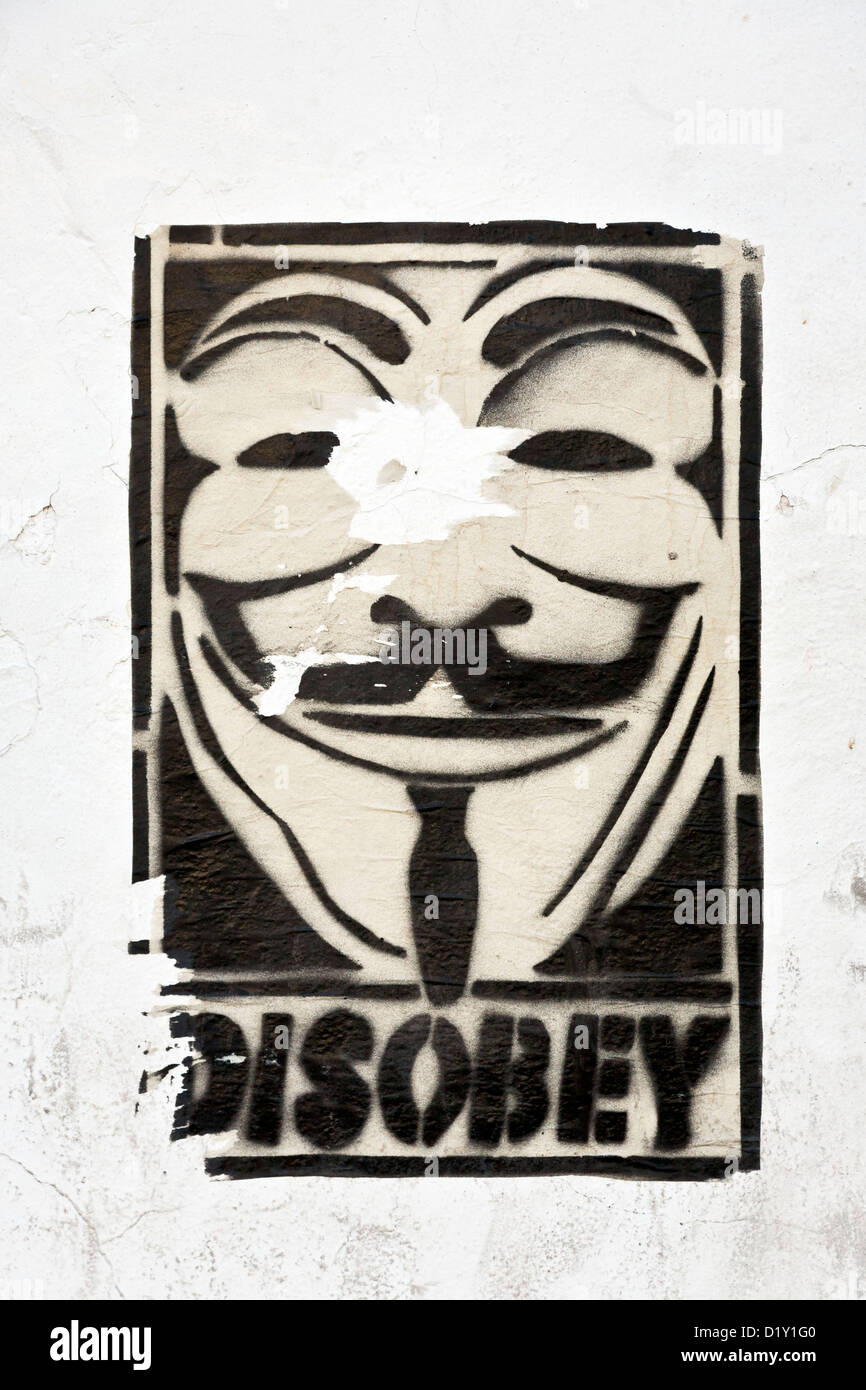 torn poster on white plaster wall of universal icon symbol of protest Guy Fawkes mask with single word DISOBEY Oaxaca Mexico Stock Photo