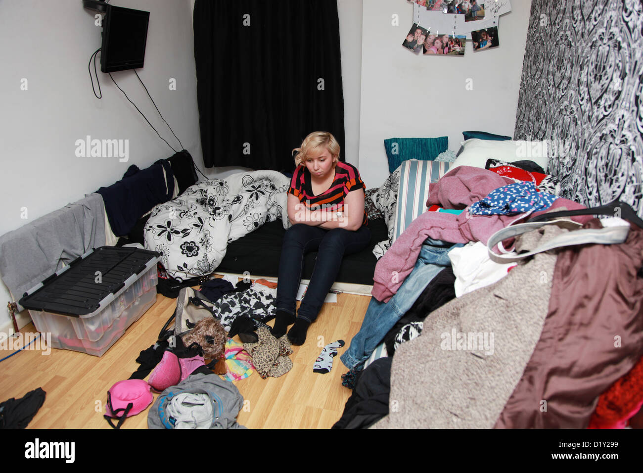 Depressed Girl Sitting On Bed In Her Messy Bedroom Stock