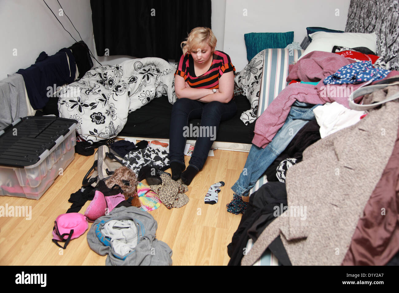 Depressed Girl Sitting On Bed In Her Messy Bedroom Stock