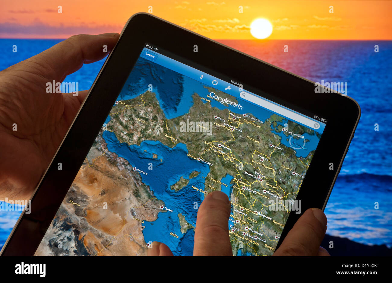 Apple iPad smart tablet with Google Earth application on screen featuring continental Eastern Europe, France Africa etc, sea and sunset in background Stock Photo