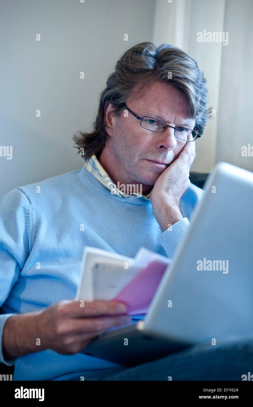 Serious mature man at home checking financial statements and bills etc on line with his laptop computer Stock Photo