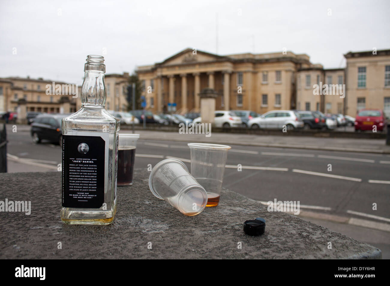 An empty discarded bottle of Jack Daniels bourbon whiskey and glasses. Hospital in background. Healthcare concept. Stock Photo