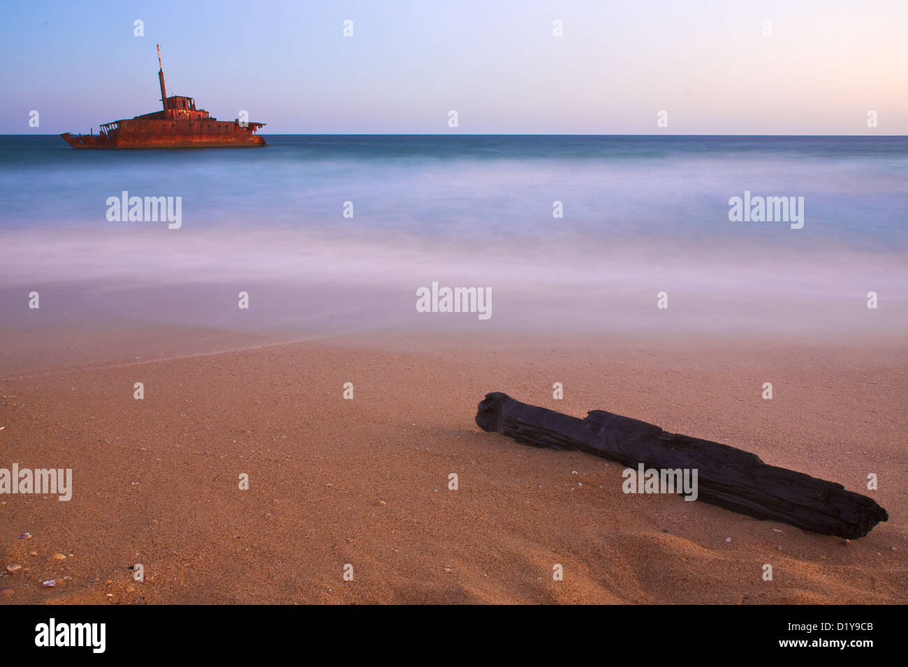 A shipwreck on the shores of a beach, with a log in the foreground Stock Photo