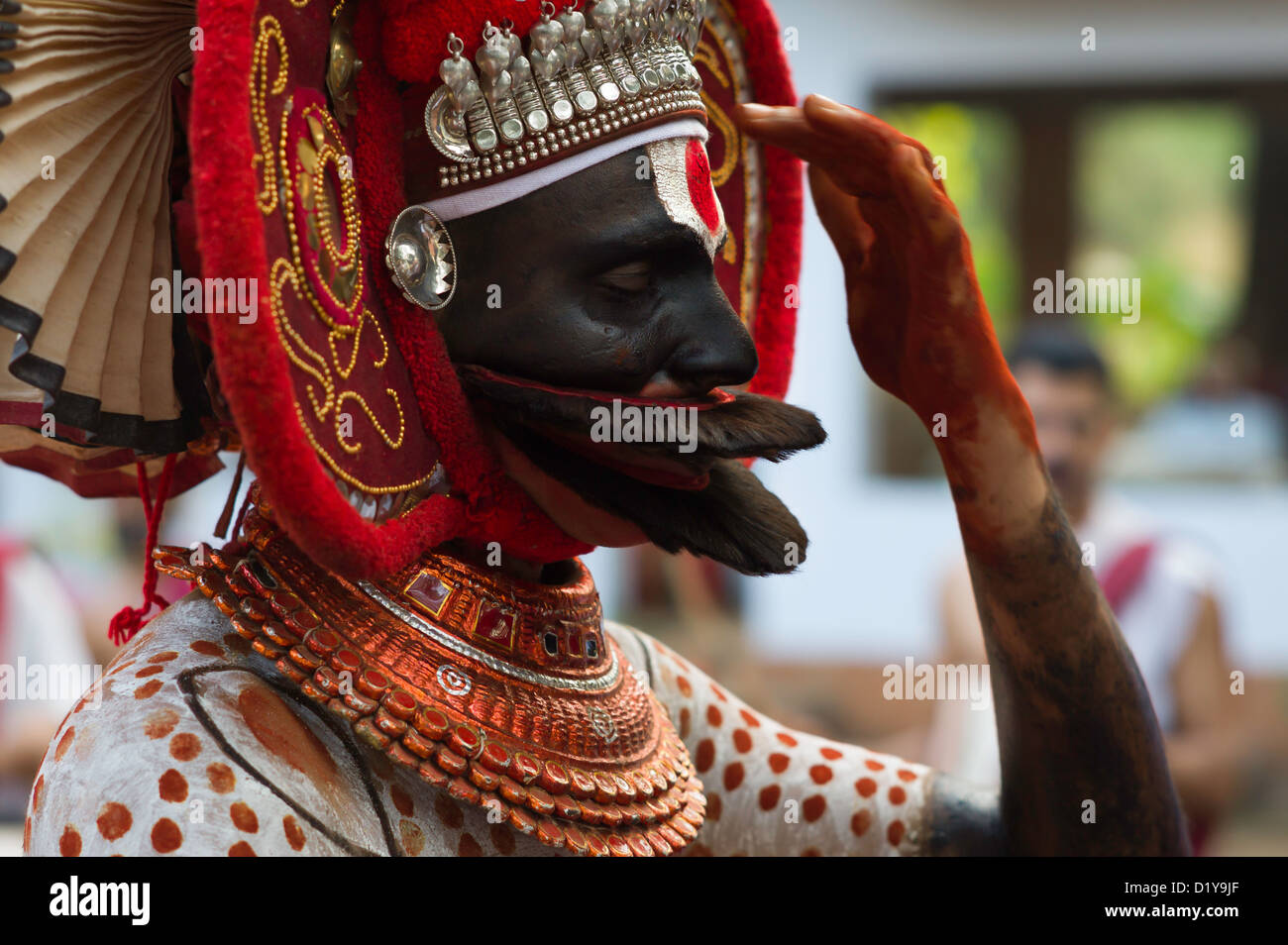 Theyyam performer in traditional costume and makeup offers a prayer to