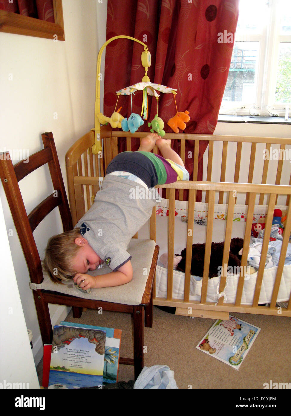 toddler climbing out of crib onto a chair Stock Photo