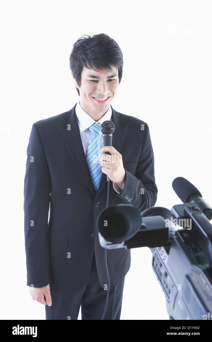 a man in a black suit speaking with a microphone in front of a studio camera Stock Photo