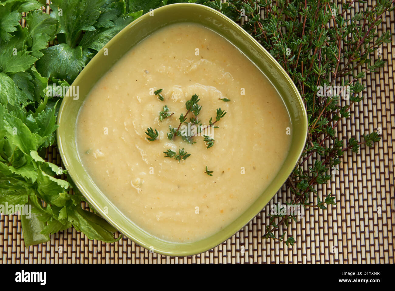 Hot cream of celeriac soup in a green bowl on the table with fresh thymus and celery. Best for autumn cold and bad weather. Stock Photo