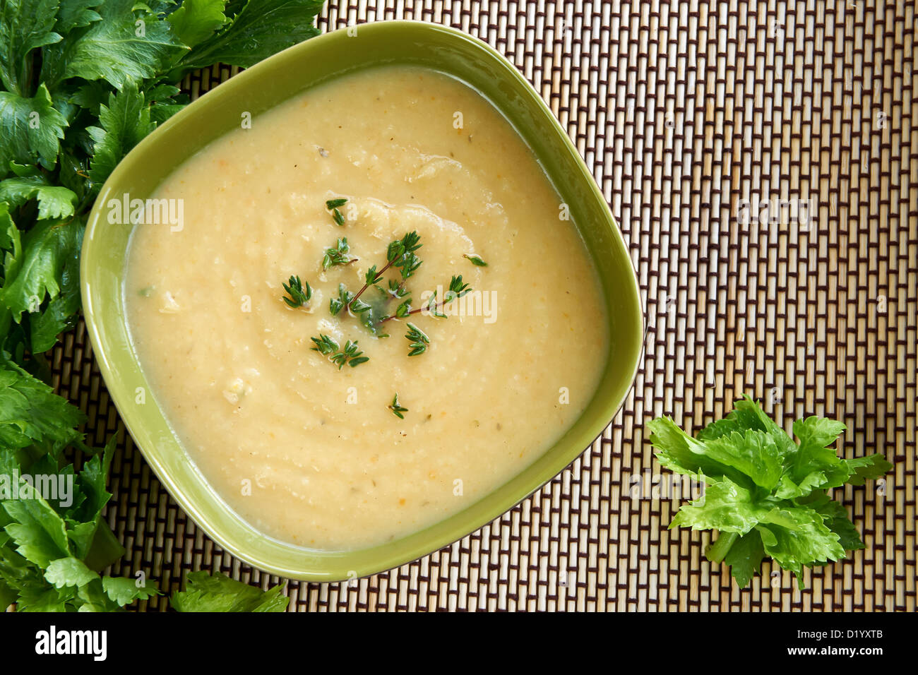 Hot cream of celeriac soup in a green bowl on the table with fresh thymus and celery. Best for autumn cold and bad weather. Stock Photo