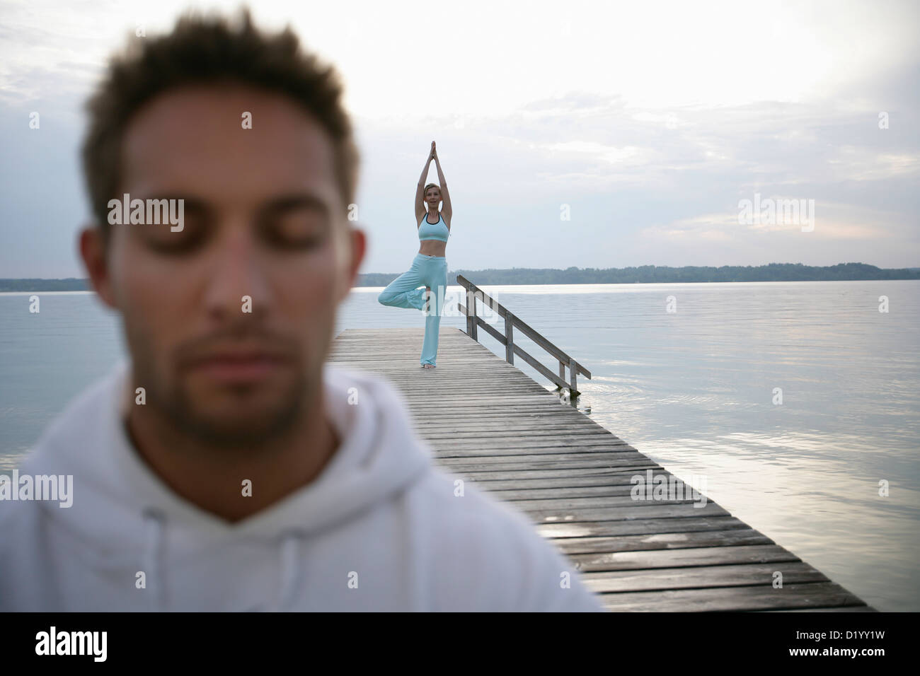 Man with closed eyes, woman practising yoga on yetty at Lake Starnberg, Muensing, Bavaria, Germany Stock Photo