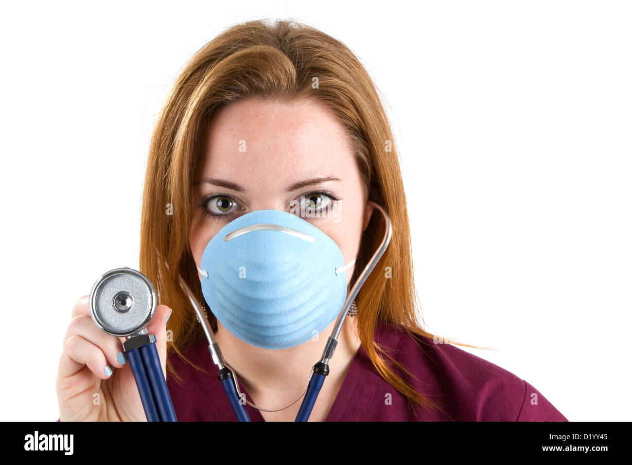 Female nurse wearing scrubs and a surgical mask holds a stethoscope. Stock Photo