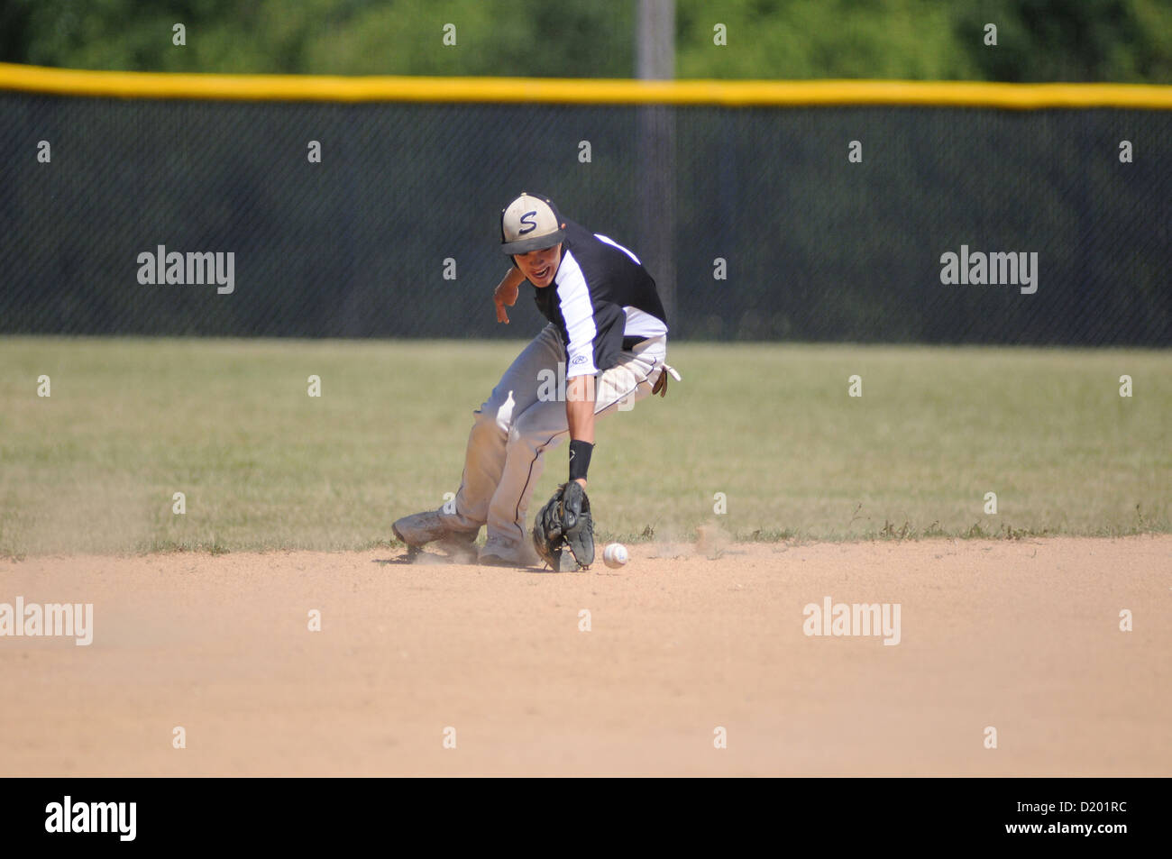 Baseball Second baseman moves behind second base to backhand a ground ball high school game. USA. Stock Photo