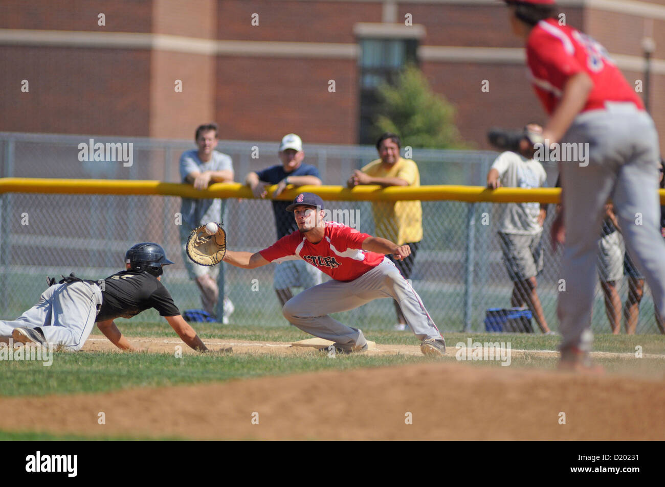 Runner dives back to the bag as first baseman reaches for a pick-off throw from his pitcher. USA. Stock Photo