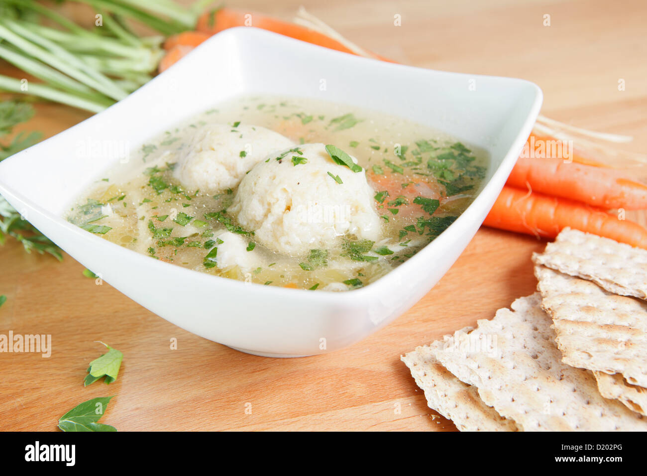 A single serving of kosher Matzah ball soup on a wooden table garnished with fresh carrots and