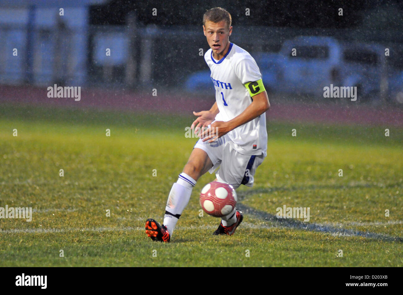 Soccer Forward works in a driving rain to maintain his footing while attempting to set up a scoring bid during high school match USA. Stock Photo