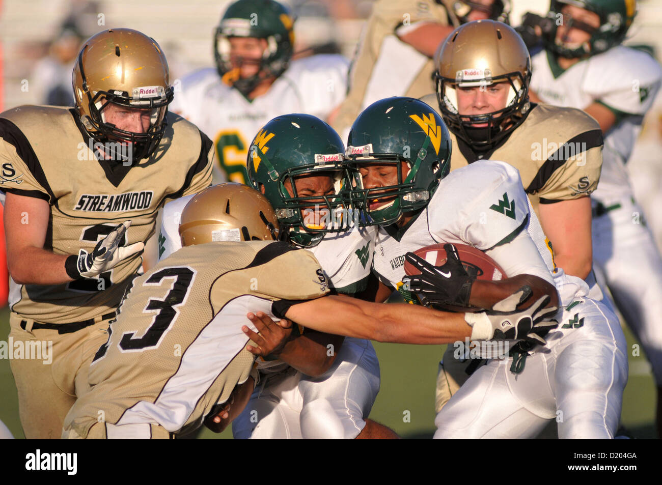 Football running back along with a blocker halted by a tackler during a high school football game. USA. Stock Photo