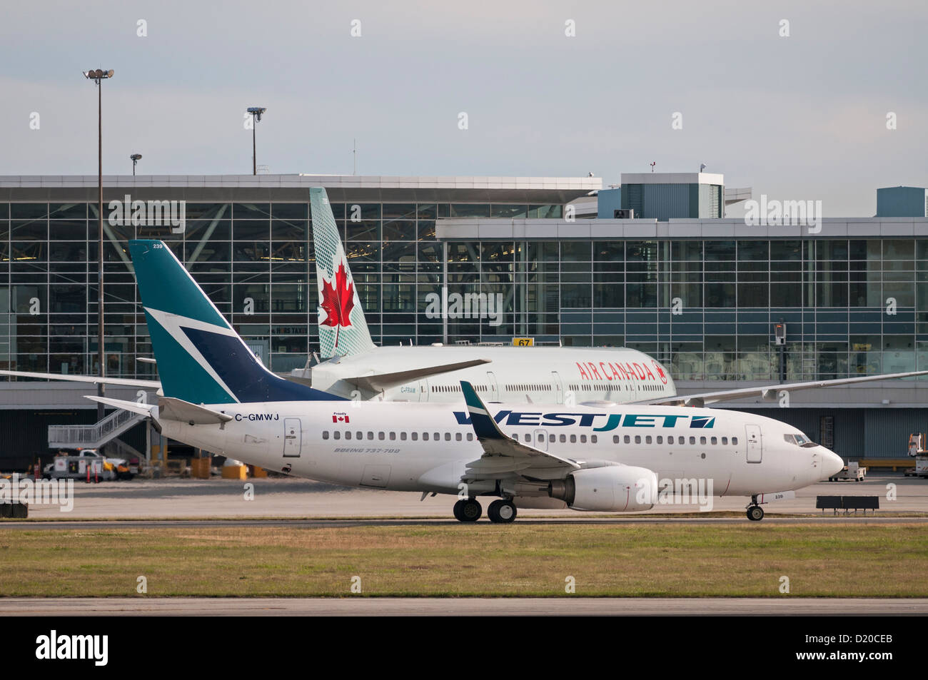 A Westjet Boeing 737 (737-700) jetliner taxies by an Air Canada Boeing 777 (777-300ER) passenger jet. Stock Photo