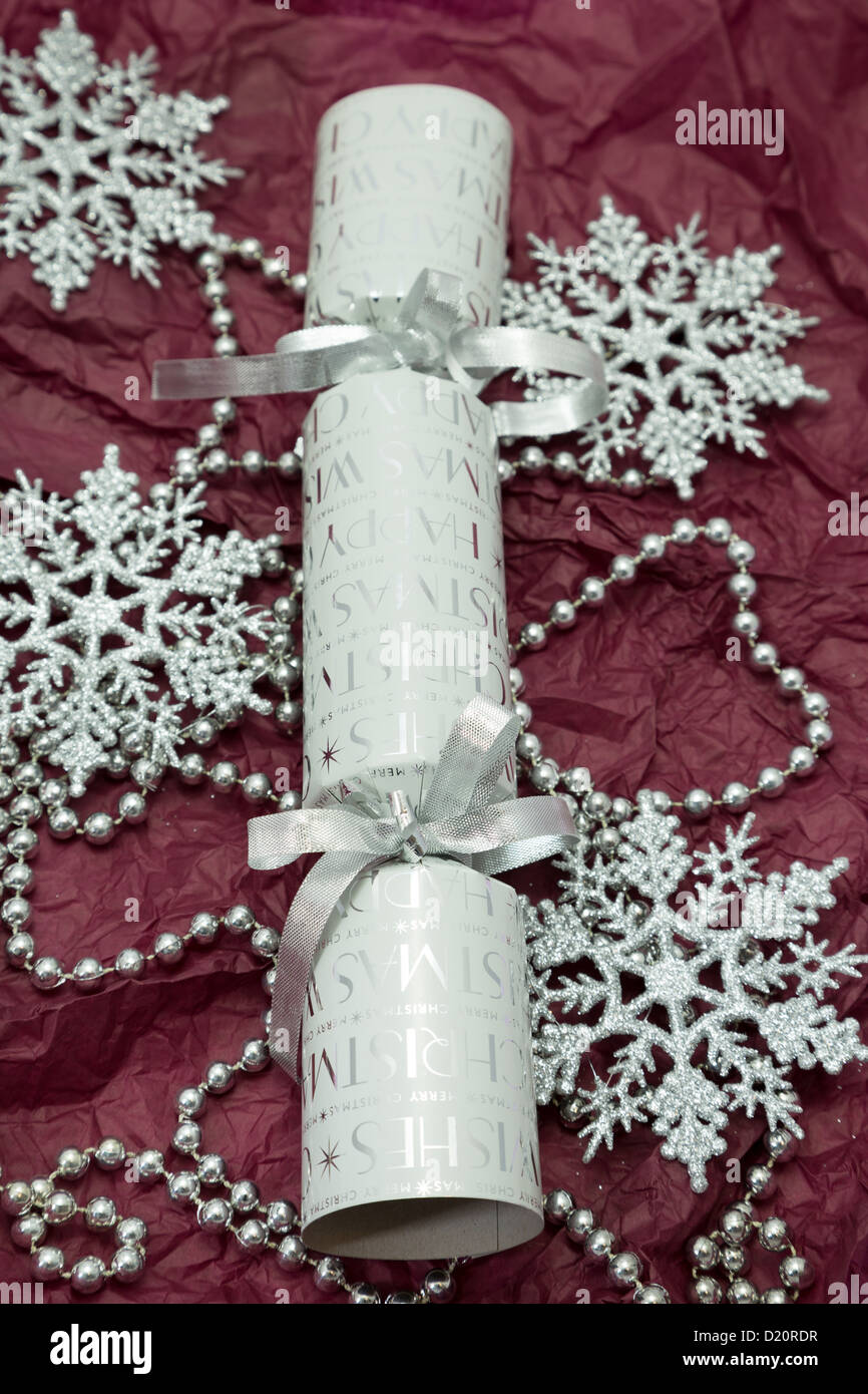 Festive silver Christmas cracker with glitter snowflake decorations on a deep red background. Stock Photo