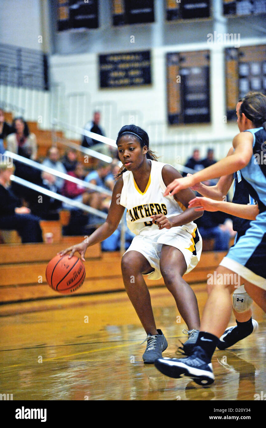 Female basketball player pulls up off her dribble as her potential path to the basket is cutoff by a defender during high school game. Stock Photo