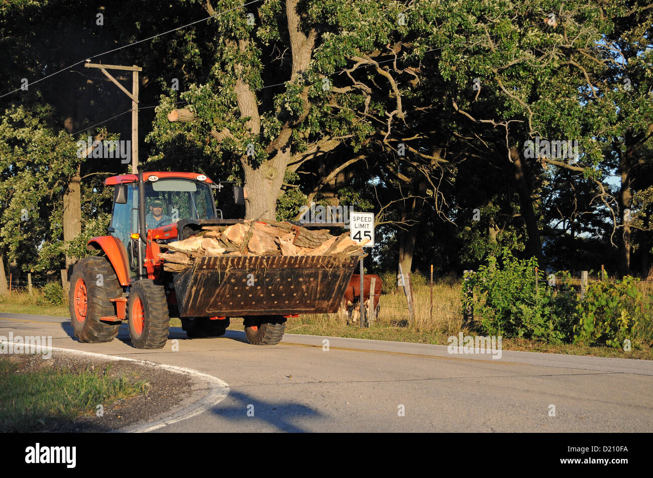 Tractor farmer moves wood slowly down a rural highway in Illinois farm country. USA. Stock Photo