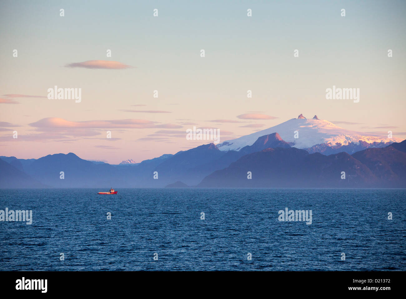 Fishing boat and snow-covered volcanic peak at sunset, Chilean fjords, Magallanes y de la Antartica Chilena, Patagonia, Chile, S Stock Photo