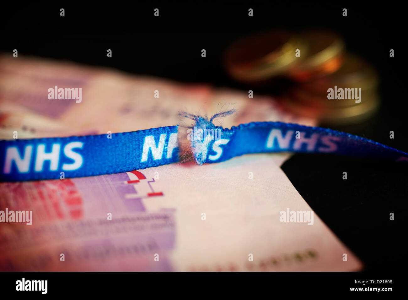 NHS neck ribbon snapped in half and fraying. laying on a bed of money, symbolizing a broken NHS health care Stock Photo