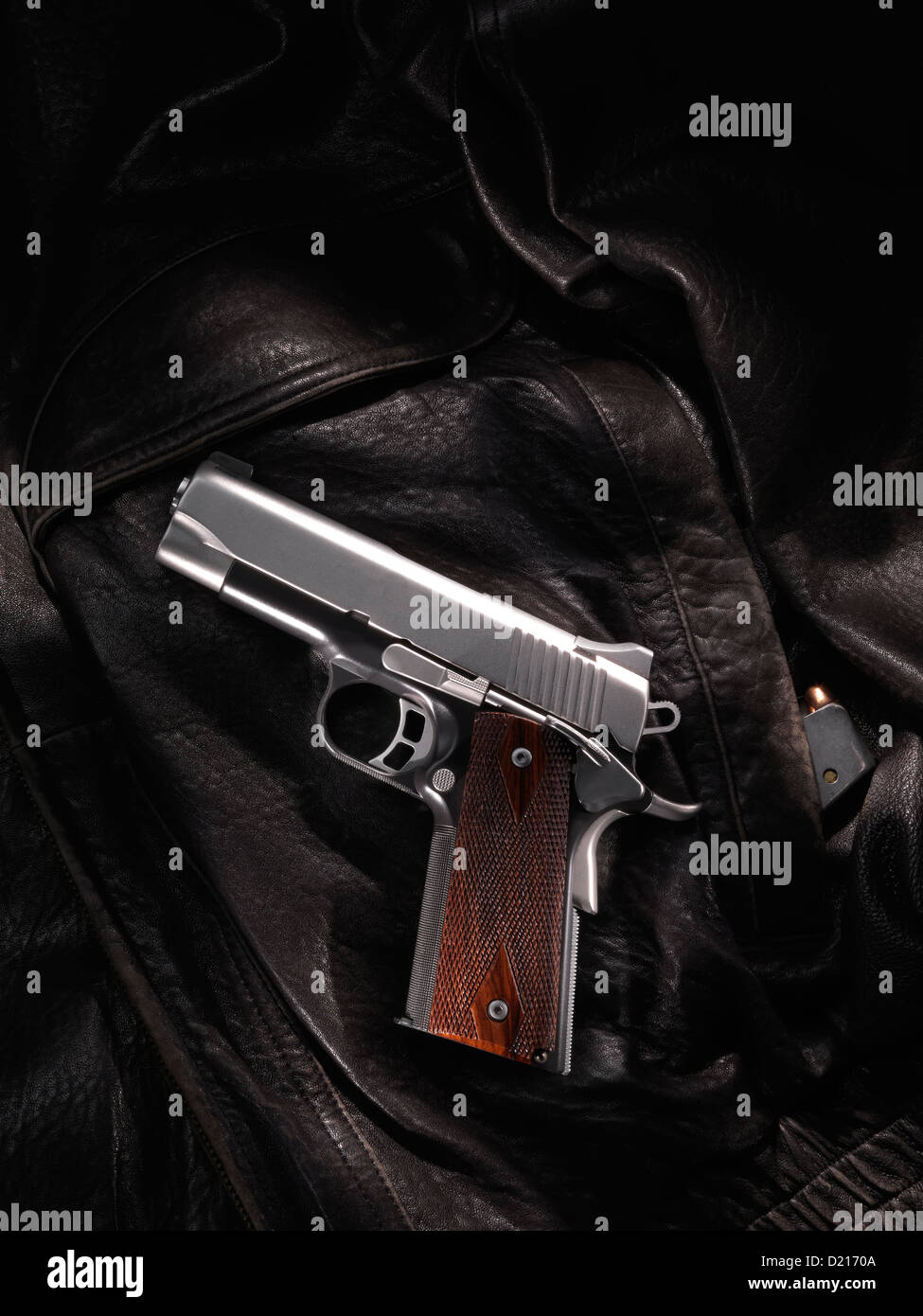 A .45 caliber automatic pistol lays on a leather coat, with an extra clip in the coat pocket