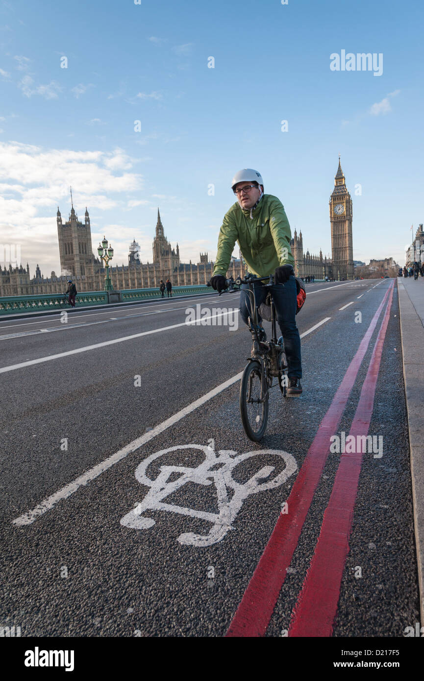 A cyclist riding on road over Westminster Bridge London UK showing cycle lane and double red lines, parliament in background. Stock Photo