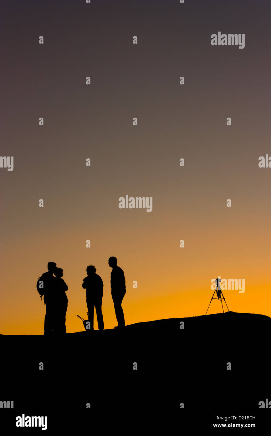 A photographer with a tripod watches a desert sunset in silhouette ...