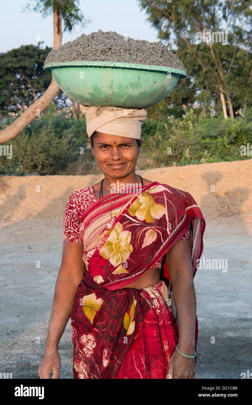 Indian woman carrying concrete in a bowl on her head whilst making concrete blocks. Andhra Pradesh, India Stock Photo