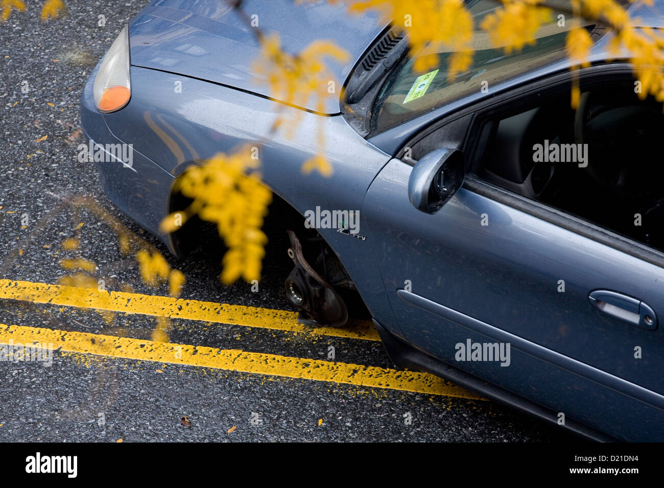 Blue Ford Taurus missing its left front wheel and lying across the middle of a divided highway. Stock Photo