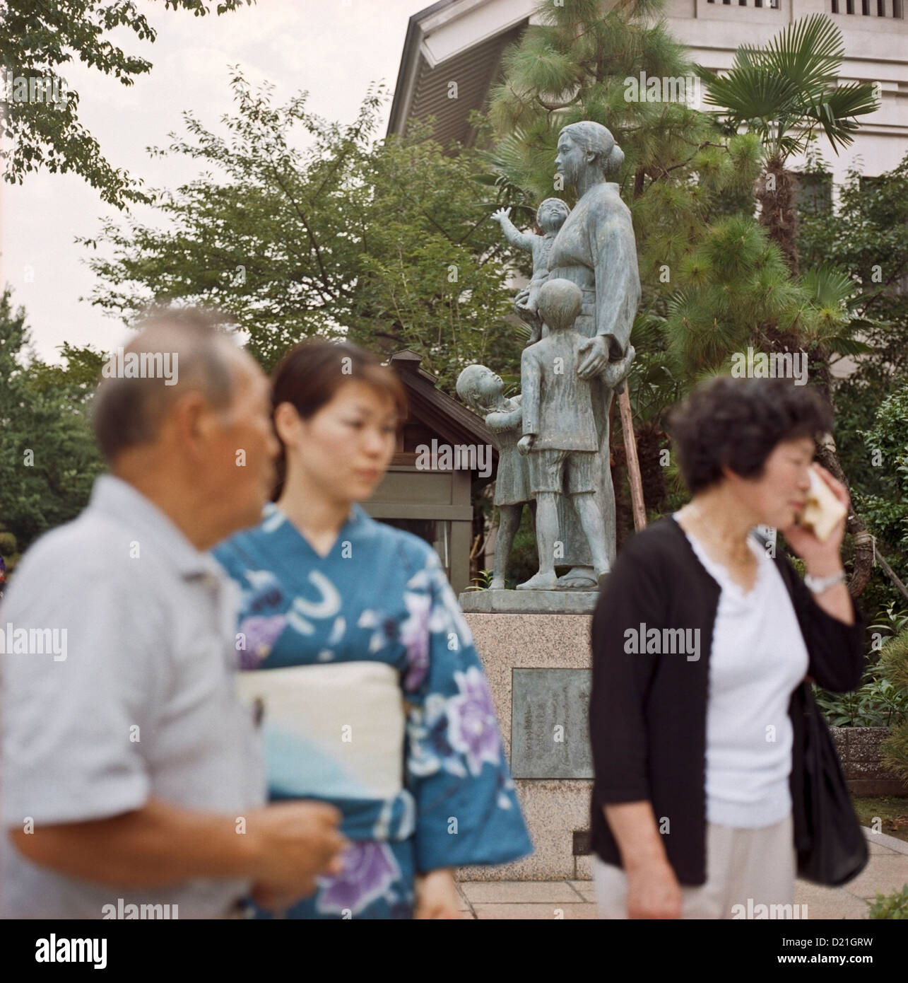 People walk by a statue of a war widow with her children at the Yasukuni Shrine in Tokyo, Japan, Stock Photo