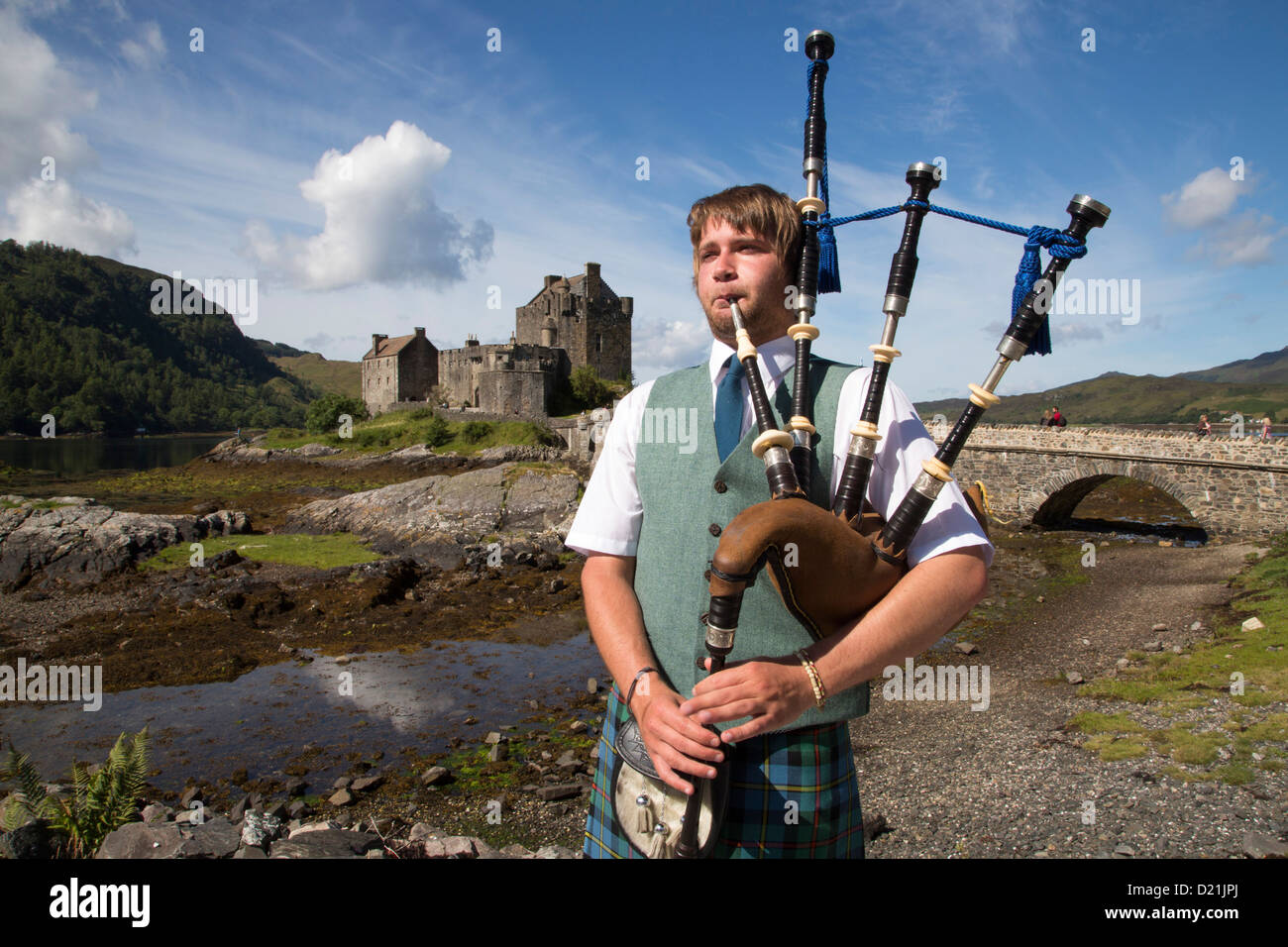 Young bagpiper in front of Eilean Donan Castle at Loch Duich, near Dornie, Highland, Scotland, United Kingdom Stock Photo
