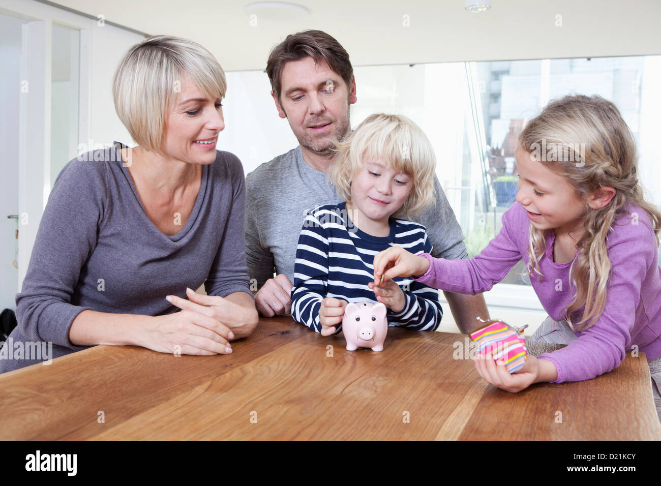 Germany, Bavaria, Munich, Child saving money in piggy bank while parents looking Stock Photo