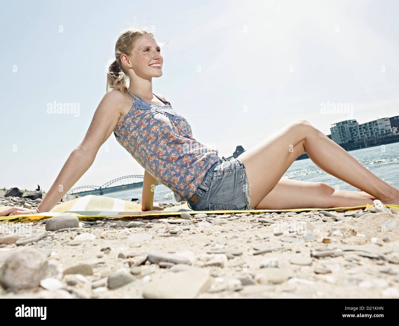 Germany, Cologne, Young woman sitting on riverbank Stock Photo