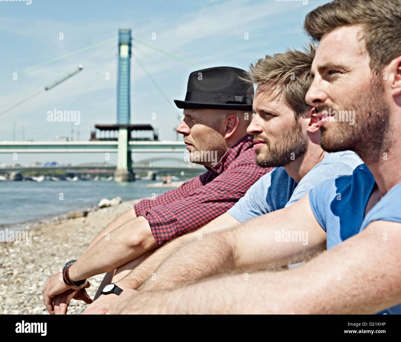 Germany, Cologne, Young men sitting on riverbank Stock Photo