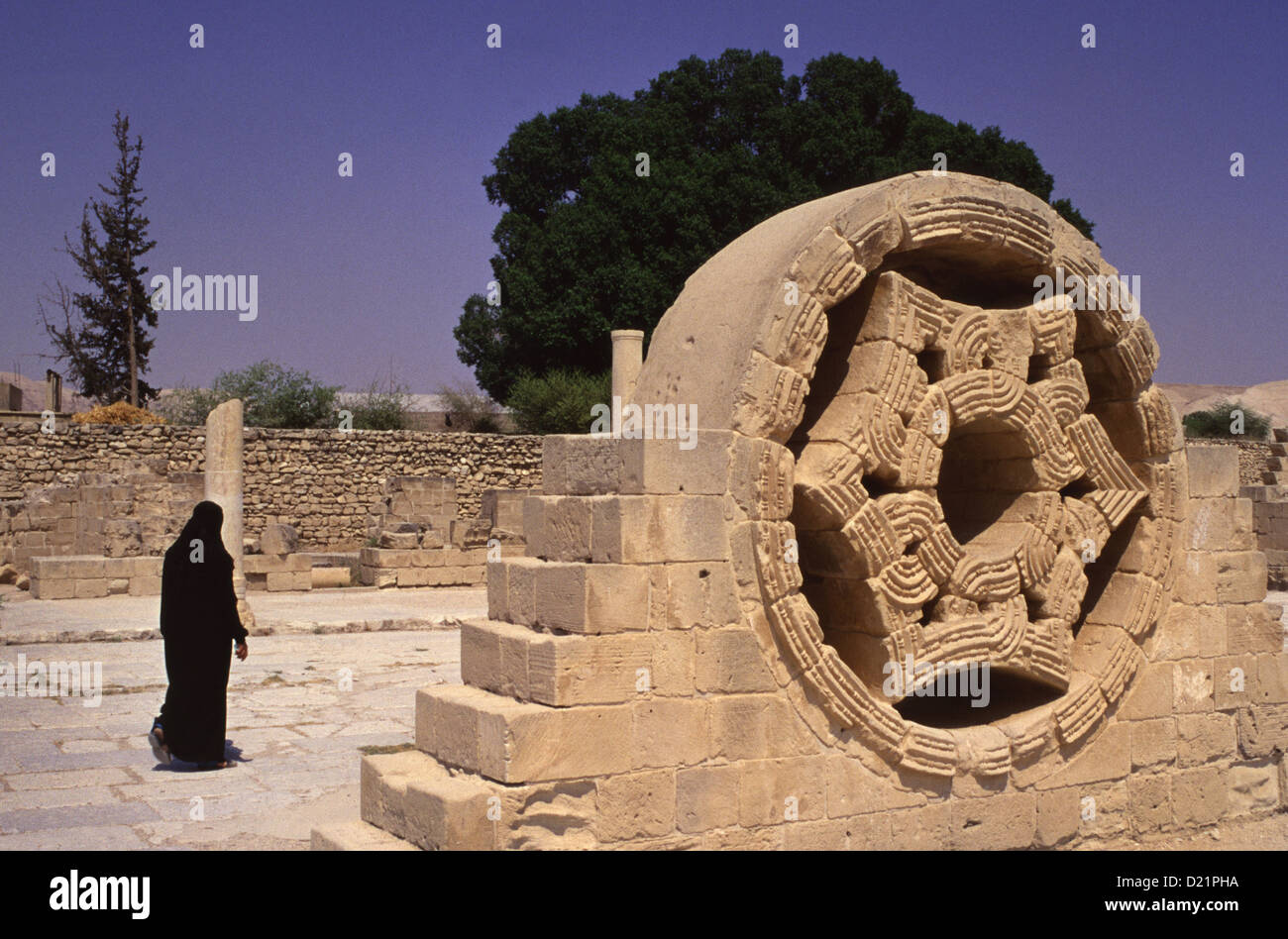 A Palestinian woman walks past a reconstructed relief ornament in Khirbat al-Mafjar popularly known as Hisham's Palace an early Islamic archaeological site near Jericho, in the West Bank Israel Stock Photo