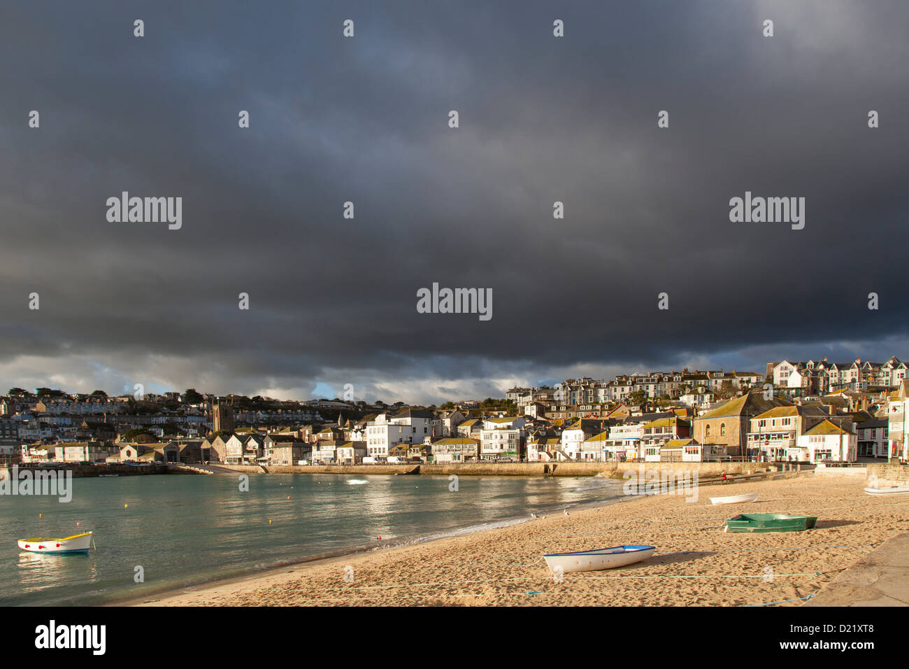 Early morning winter light illuminates buildings around St Ives harbour, whilst dark rain clouds provide an atmospheric backdrop Stock Photo