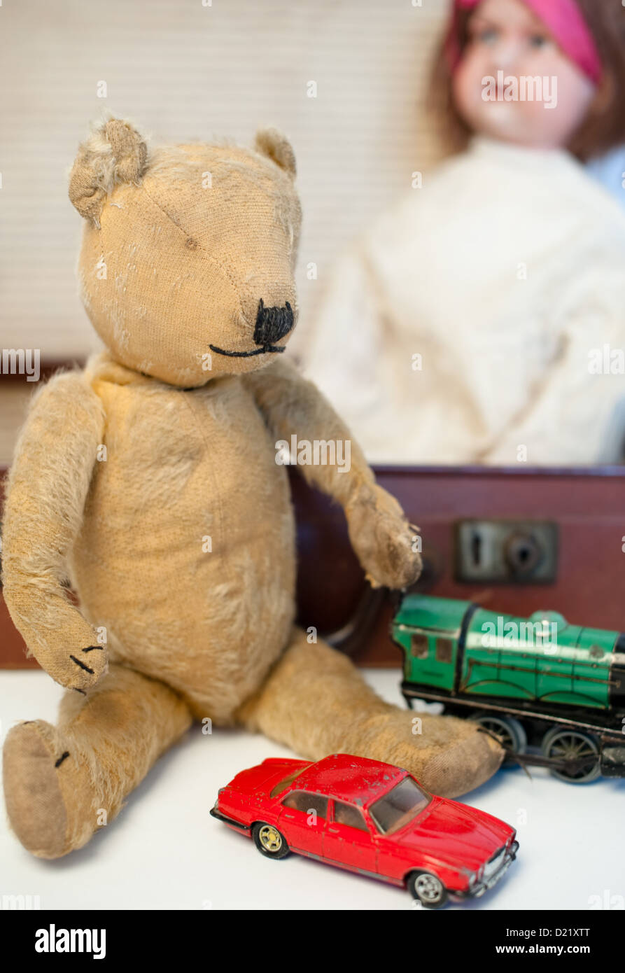 Old-fashioned well-loved vintage teddy bear, a red boys battered dinky car, green train engine and a Victorian china doll Stock Photo
